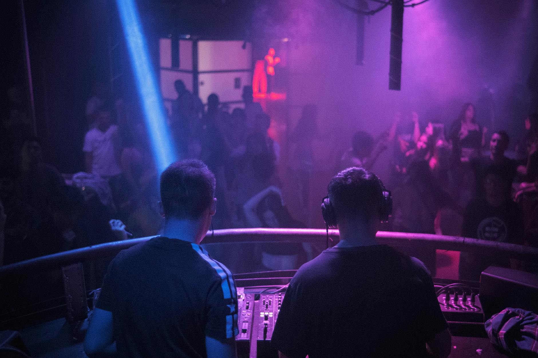 DJ gra set w klubie, kolorowe światła i tańczący tłum